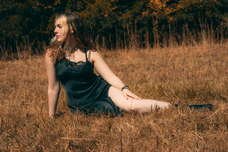 a woman in a dark dress sitting on a brown grass field