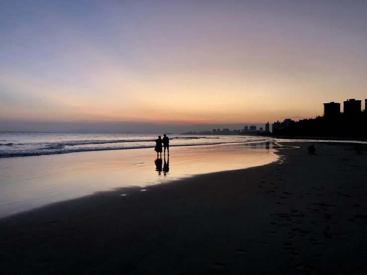 two people standing on the beach at sunset