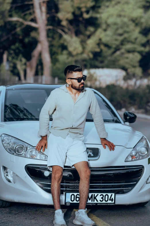 a man in white sitting on the hood of a car