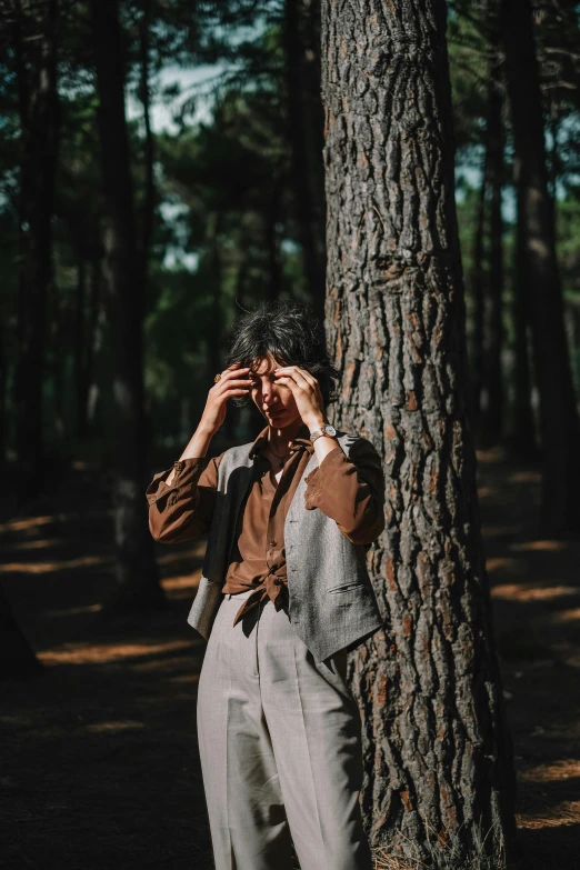 a young man standing by a tree with his hand on his face