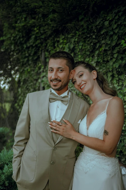 a smiling bride and groom posing in front of greenery