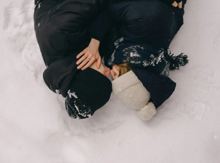 two people wearing warm clothing rest on the snow