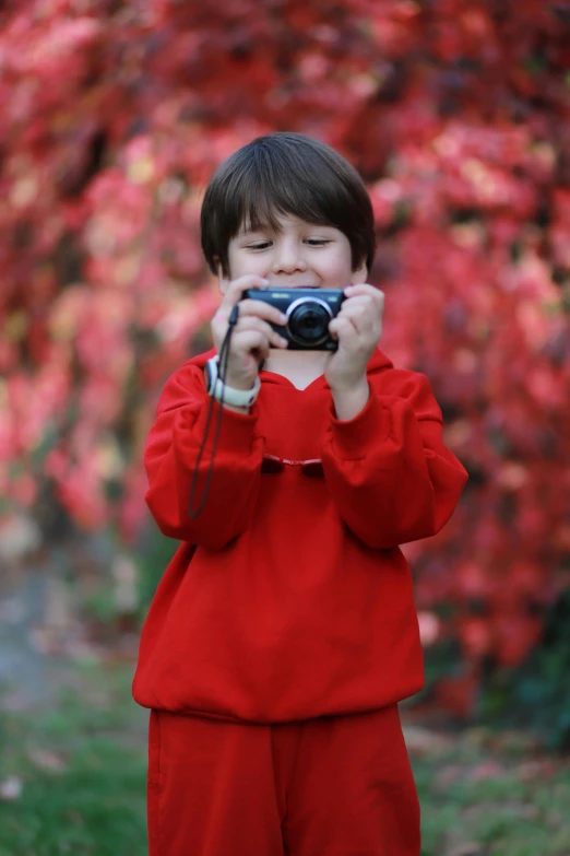 a little  in red taking a picture with a camera