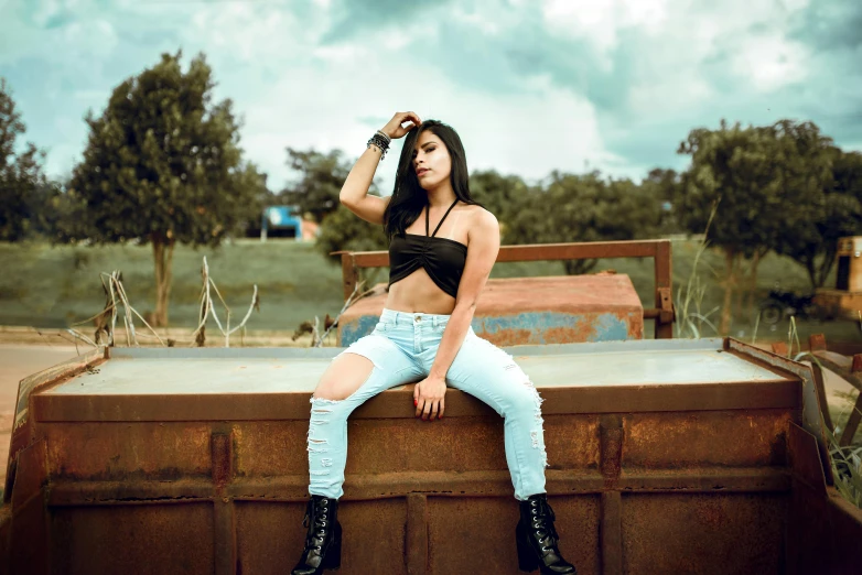 a woman in jeans sitting on top of an old rusted truck