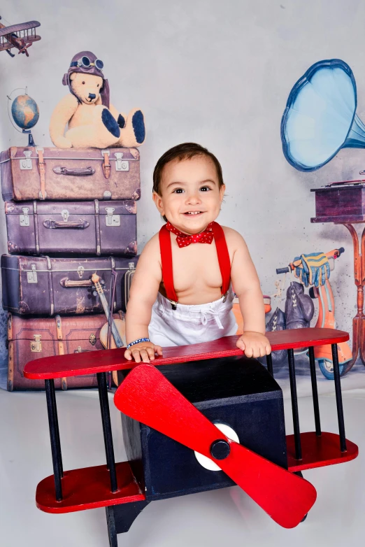 a baby sitting on top of a red toy airplane