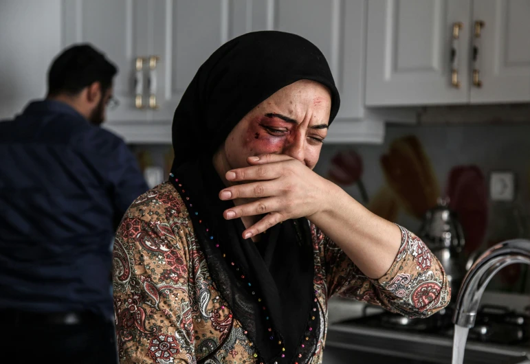 a woman covers her face with her hands while standing near a kitchen counter