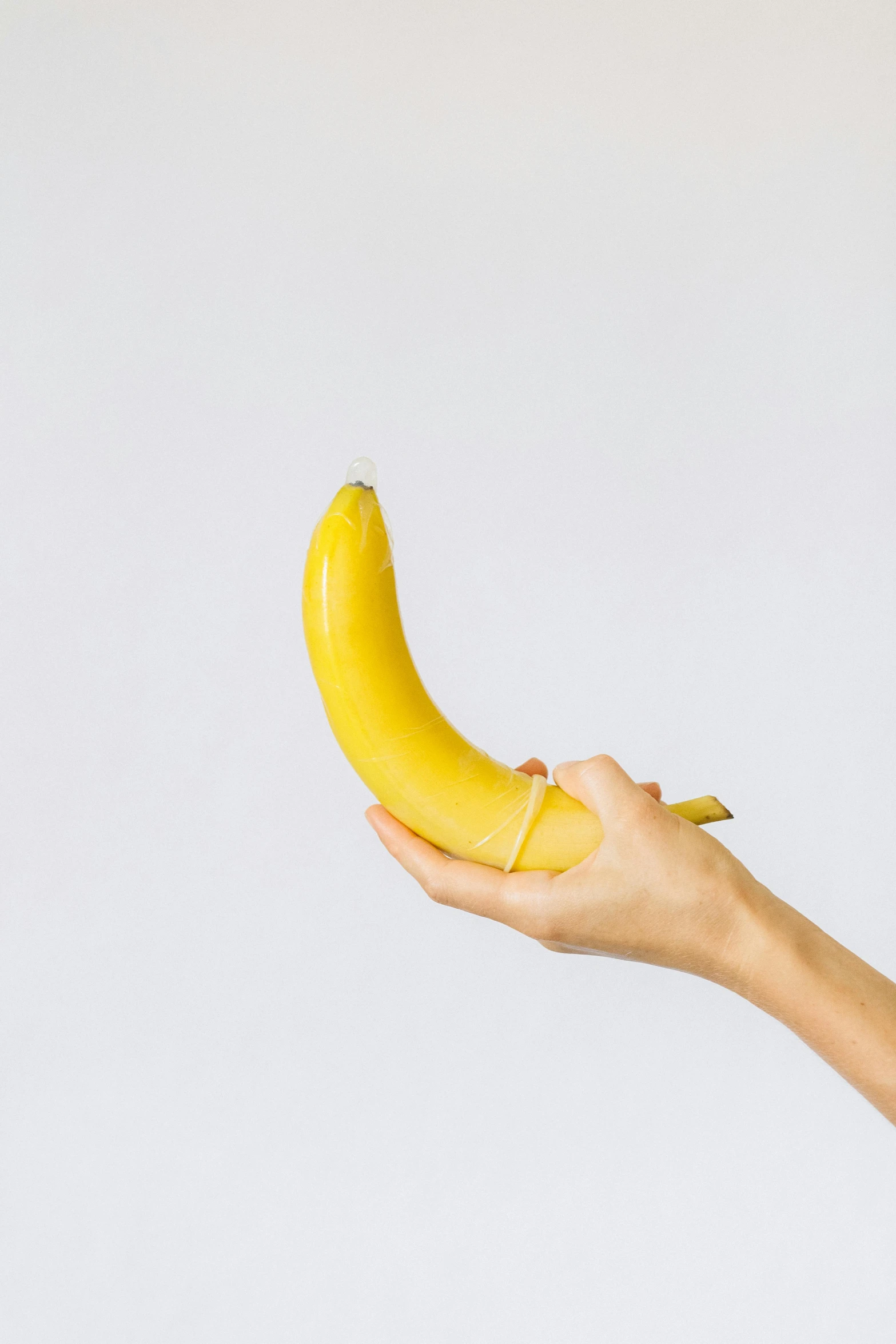 a hand holding a banana on top of a white wall