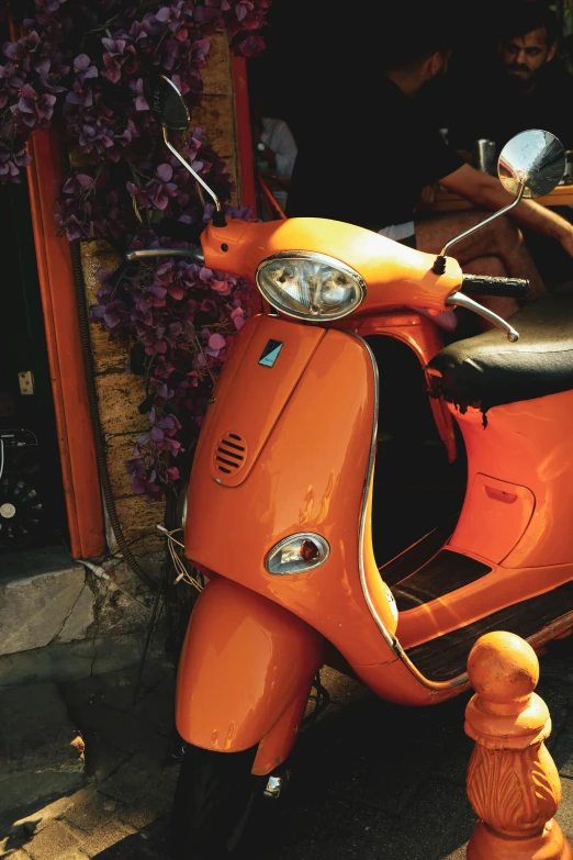 an orange scooter is parked near some flowers