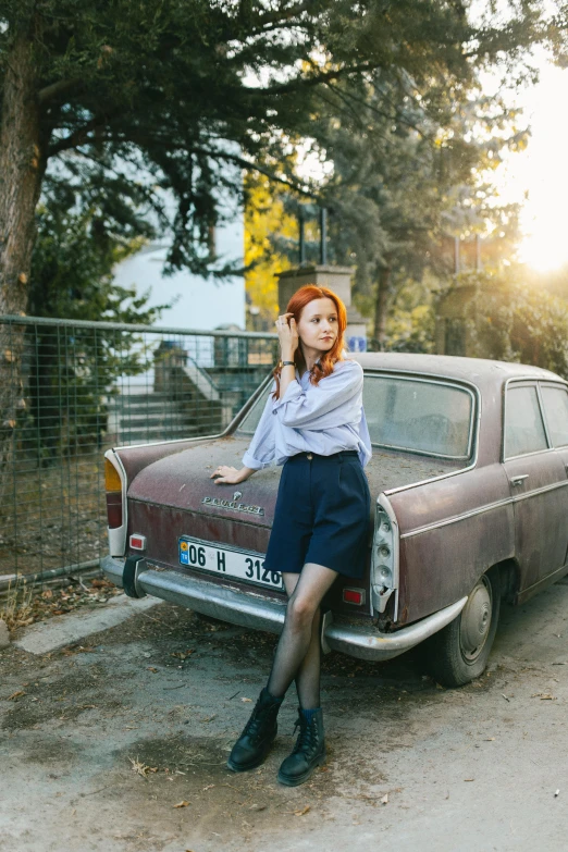 the redhead woman sits on the bumper of an old car