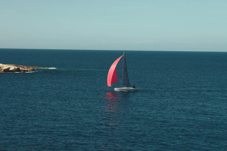 a red sail boat on open ocean water