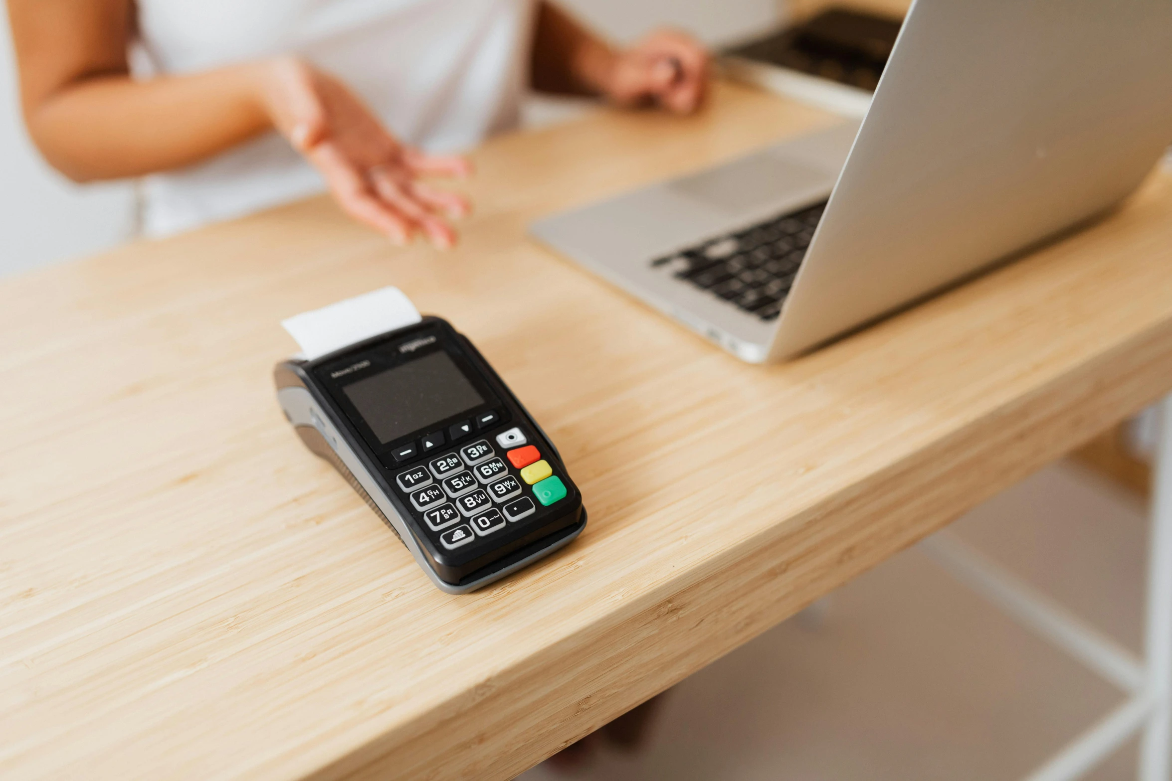 a person sitting at a wooden table with a cell phone next to a laptop