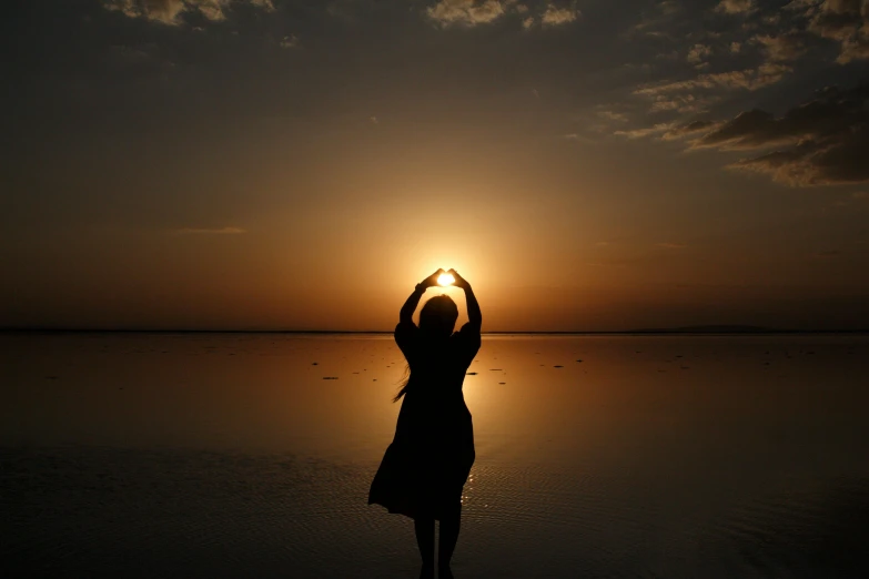 a silhouette of the sun at a beach, with a person doing a hand - sign