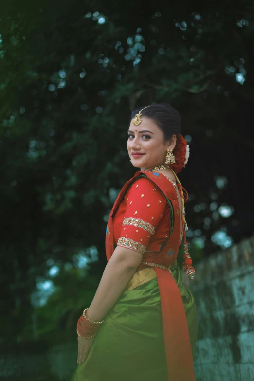 a girl in a saree, standing by a tree