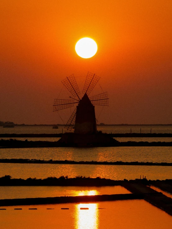 the sun is setting behind a windmill over water