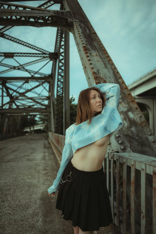 a girl standing outside with her hair in a ponytail and looking out a metal fence, on a bridge