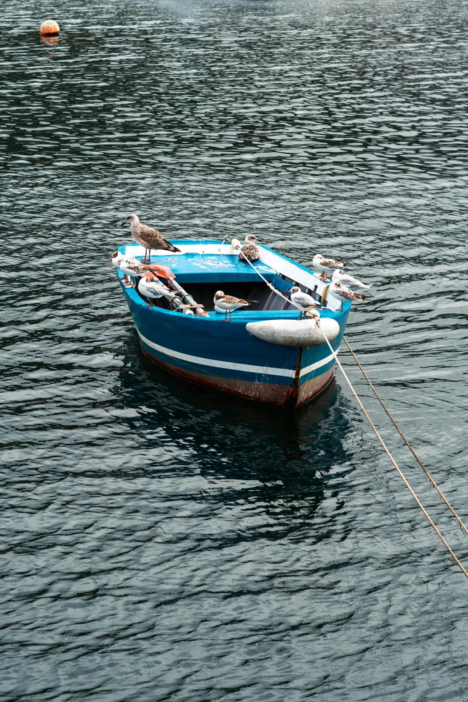 a small blue boat with two passengers tied to a pole in the water