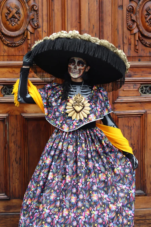 a woman with a skull makeup and black hat with yellow ribbons, with a fan on her head