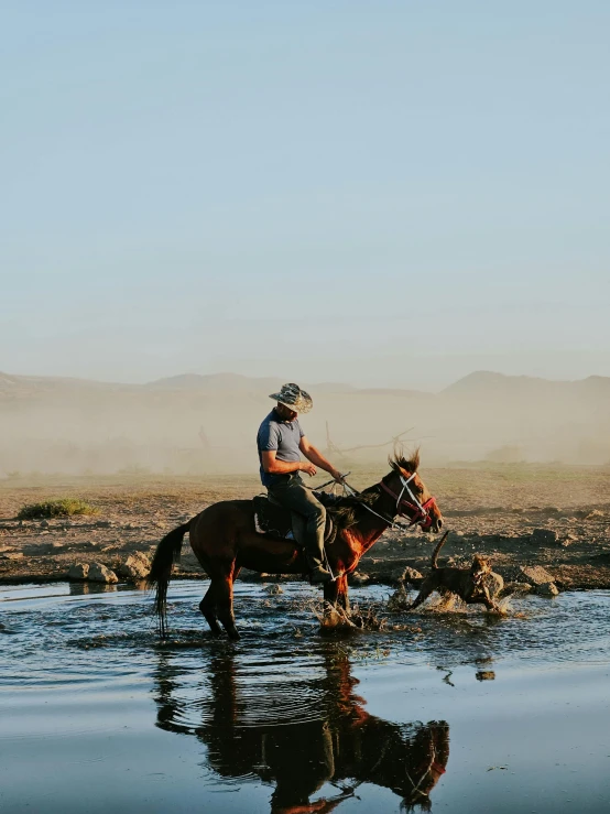 a man on horseback crossing a creek while the water rises