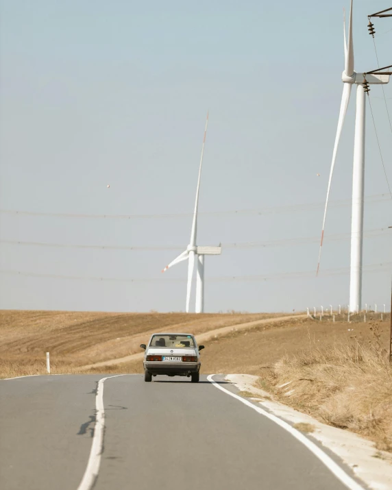 car traveling down the road next to wind turbines