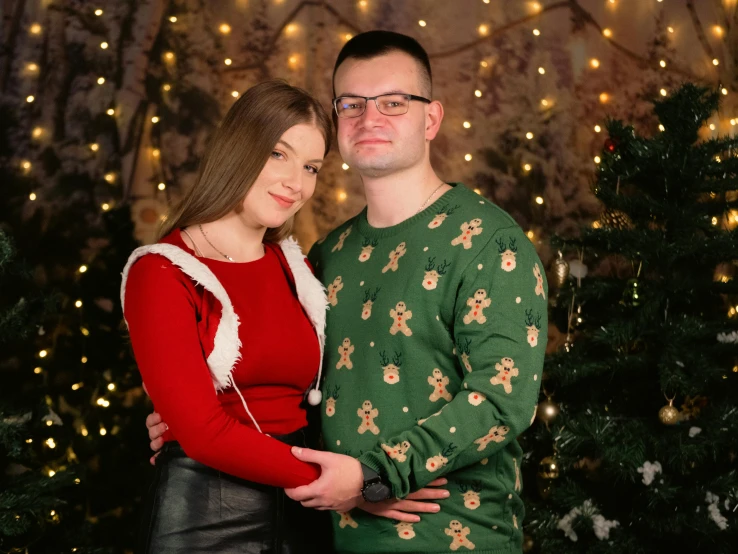 man and woman in christmas pajamas standing in front of a lit up tree