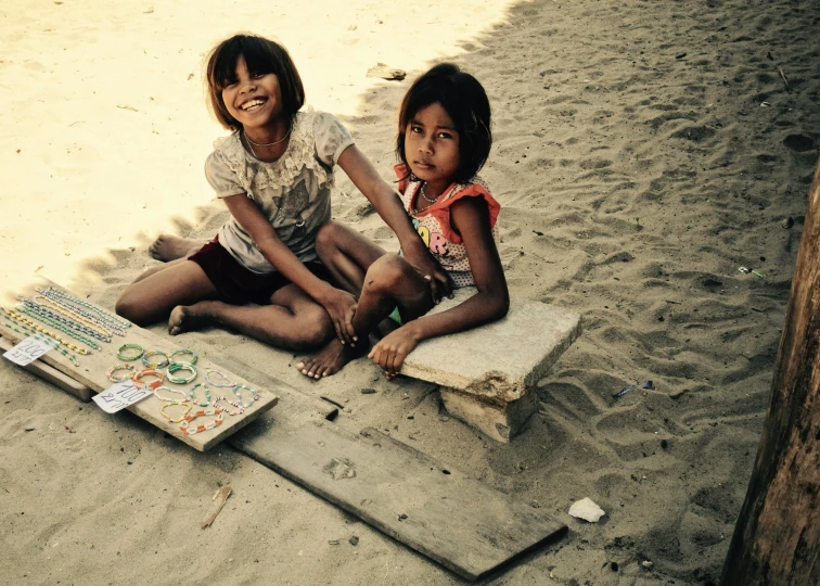 a couple of little girls sitting on top of a sandy beach