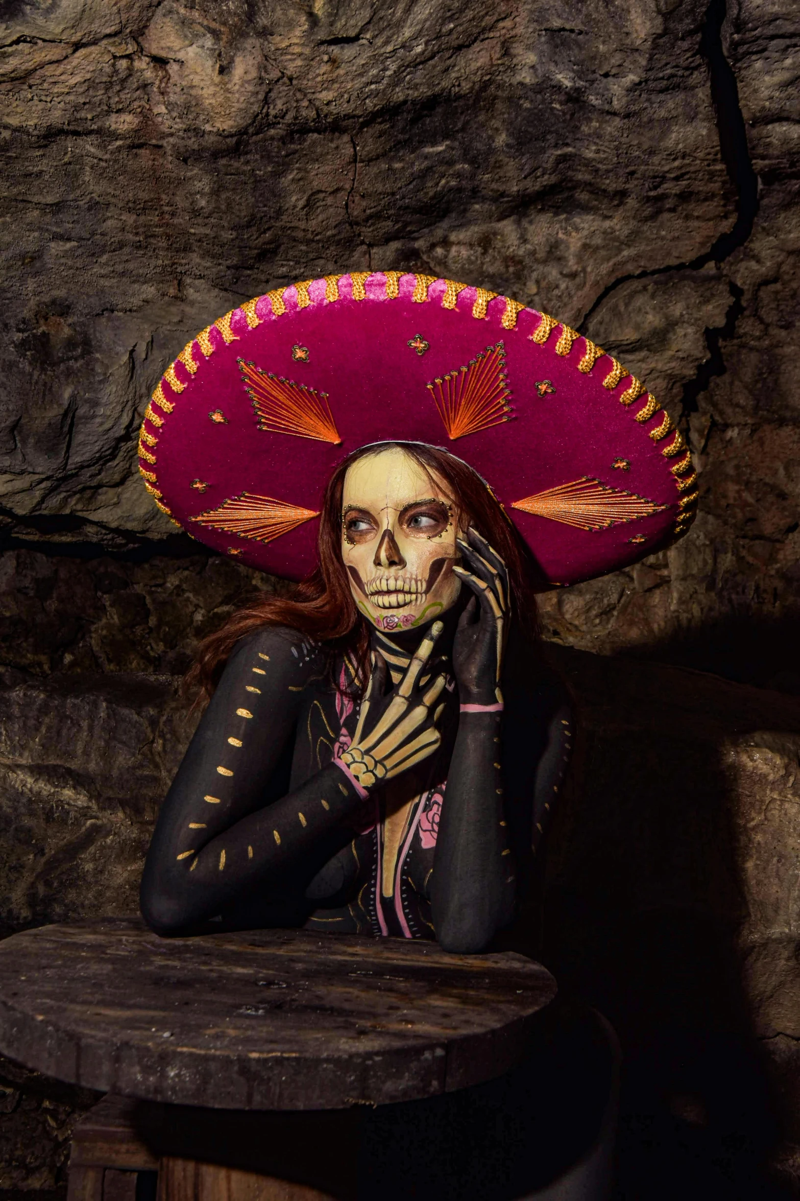 a woman in skeleton makeup and a mexican head dress holds a cell phone up to her face