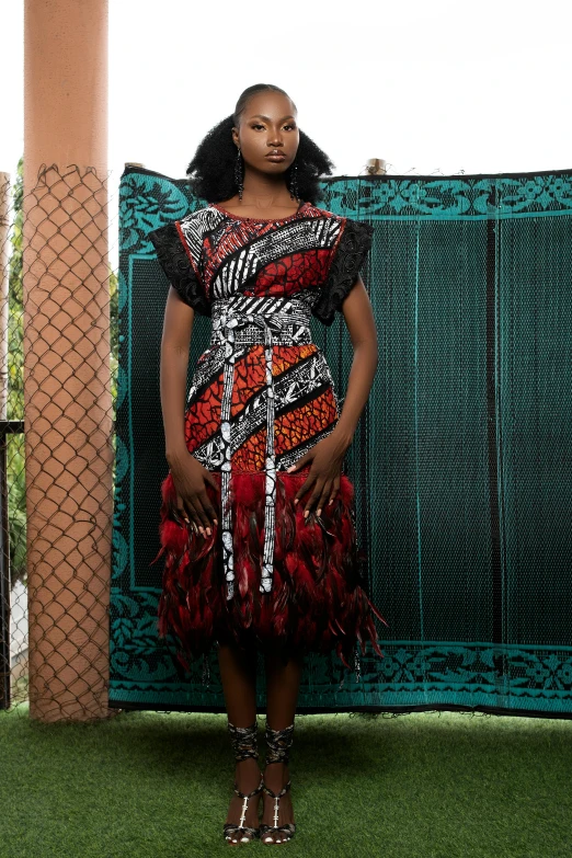 a woman poses in a multicolored dress in front of a fence