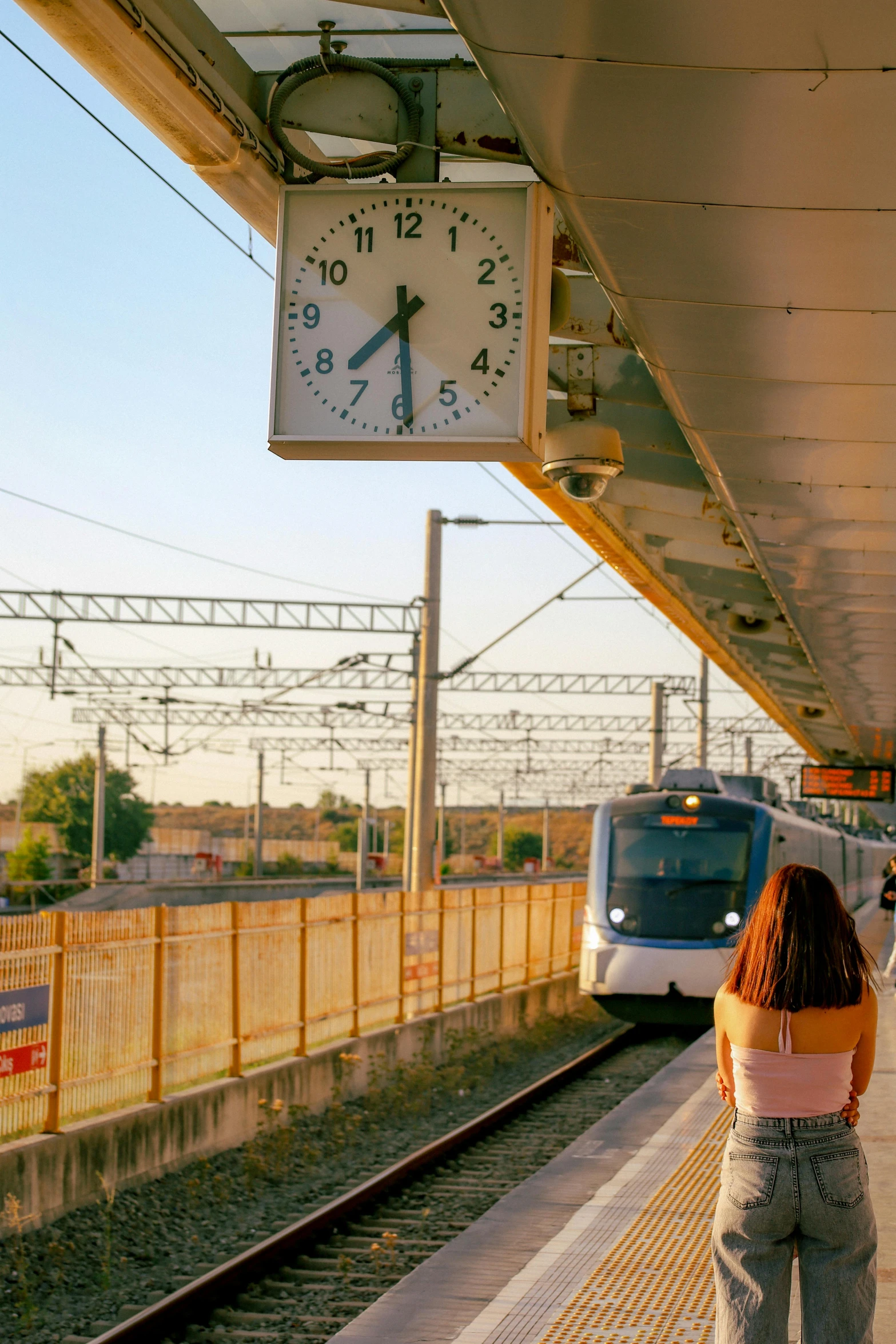 a woman standing on a rail station while watching a train