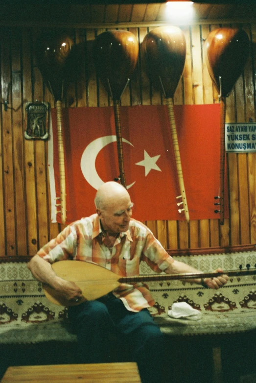 a man sits playing a guitar in front of a turkish flag