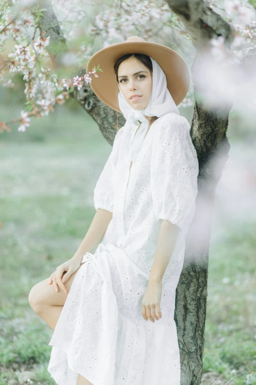 a girl in a white dress and floppy hat sitting on a tree nch