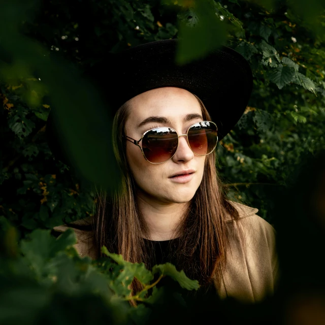a woman wearing sunglasses and a hat under some trees