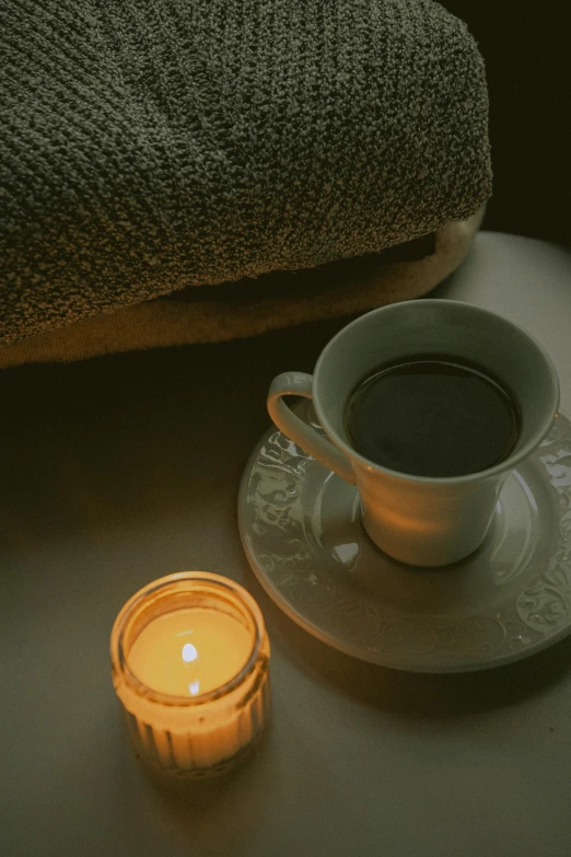 a cup and saucer with a lit candle sitting on a table