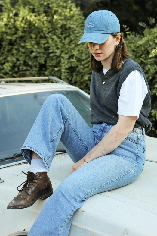 a woman wearing blue jeans and a baseball cap sitting on the hood of a white truck