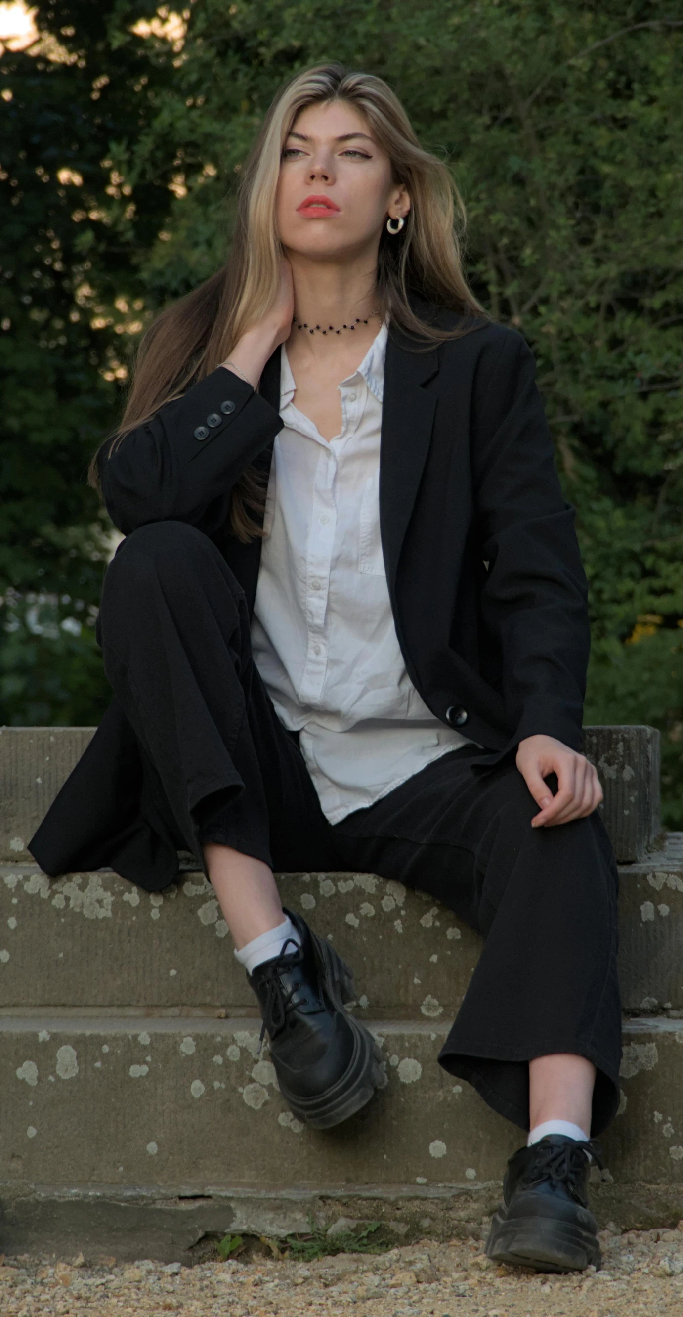 a woman sitting on top of a cement ledge next to trees