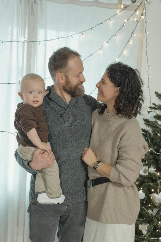 a man and woman standing near a christmas tree holding their child