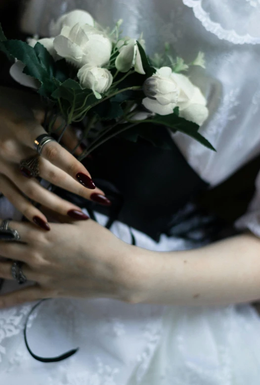 woman wearing wedding band holding white flowers and nails