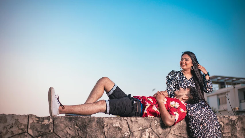 a young woman and man laying on the edge of a wall