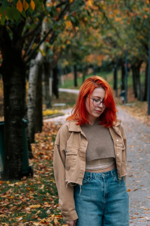 a woman with red hair and glasses stands on the sidewalk in a park