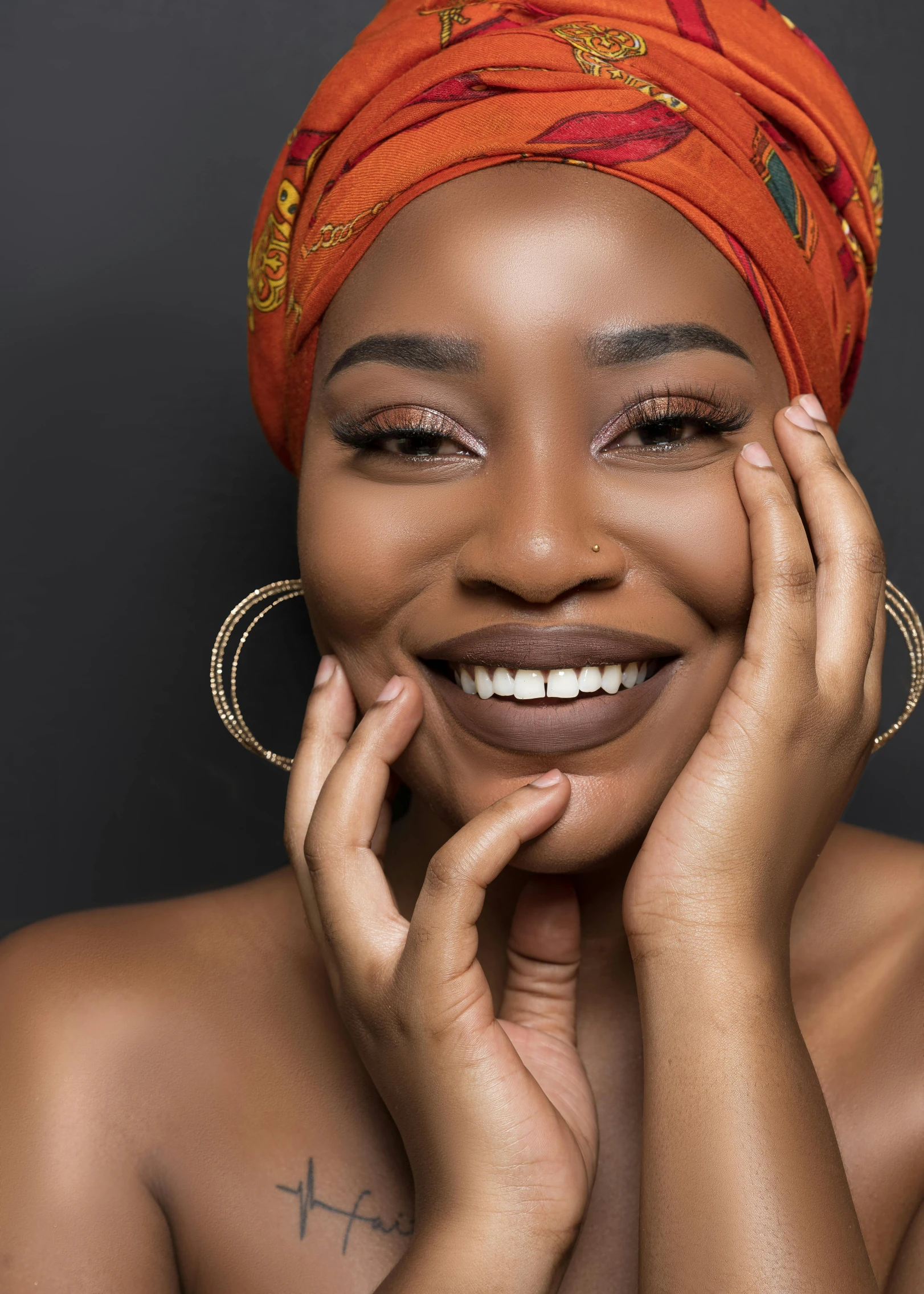 a woman smiling and wearing earrings with an orange turban