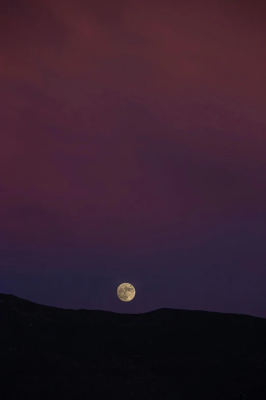 the moon is seen from the horizon above mountains