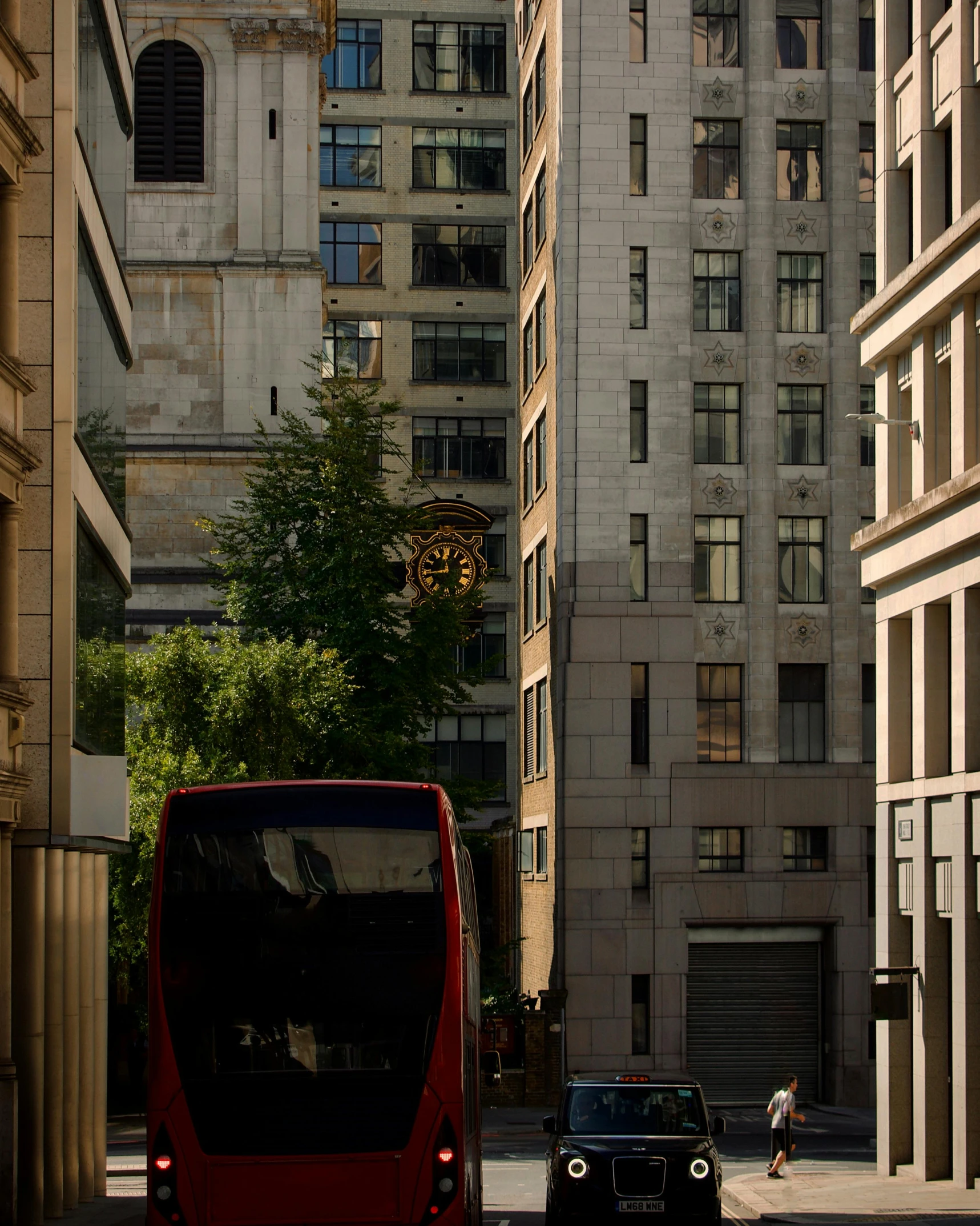 a two tiered red bus and car driving past tall buildings