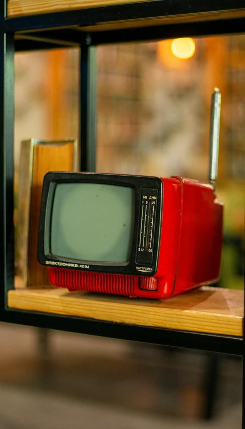 a small television with red case sits on a wooden shelf
