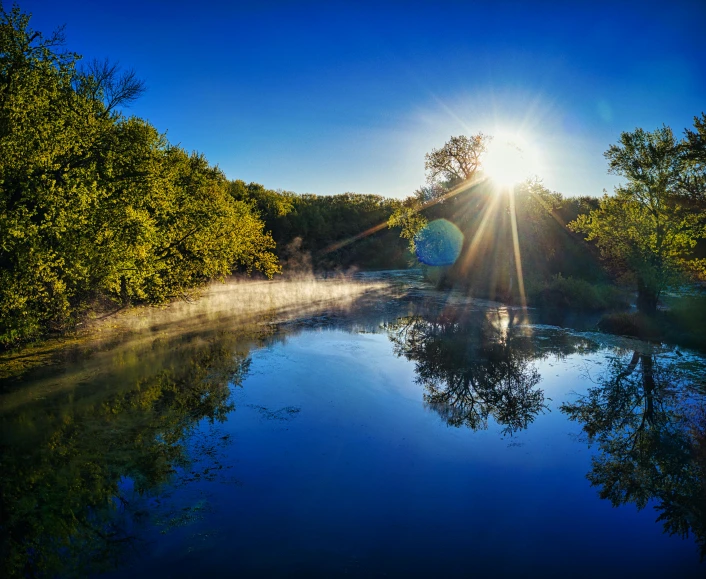 sun shining over a river surrounded by forest