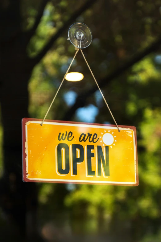 a yellow sign saying we are open hanging from a hook