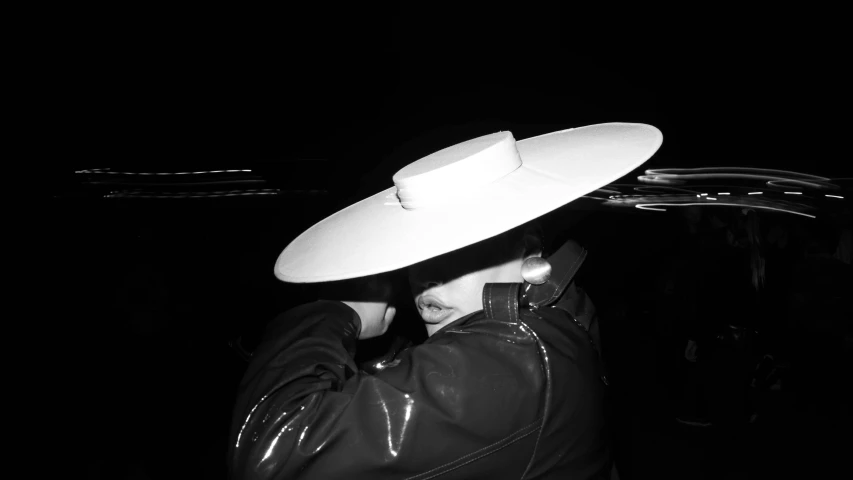 a man in black jacket and hat on dark background