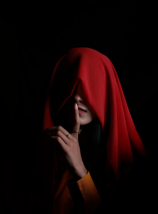 a young lady dressed in a bright red headdress is praying in a dark room