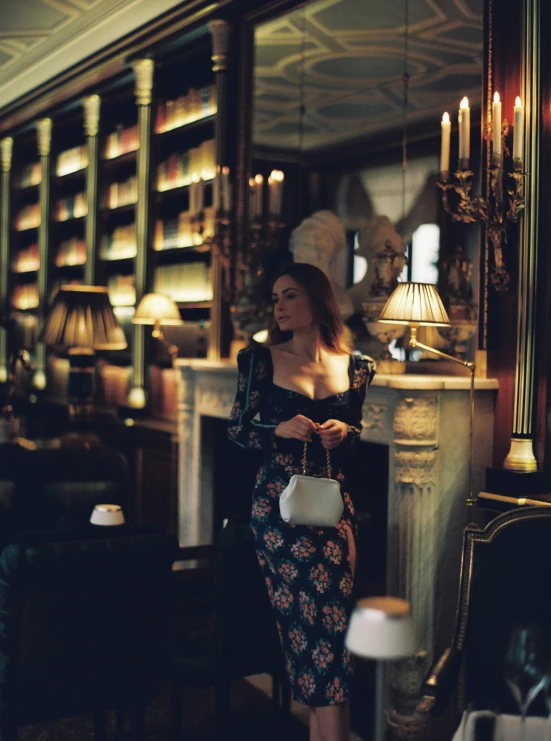 the woman stands near a fireplace in a fancy room