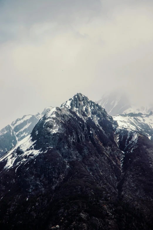 two snow capped mountains with trees below and clouds overhead