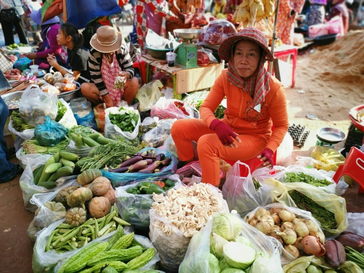 a lady wearing a hat sits amongst many fruits and vegetables