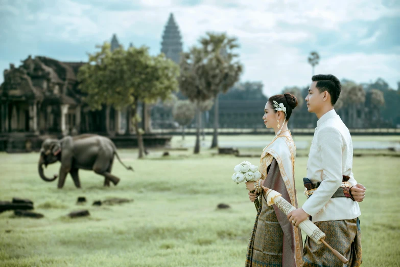 asian couple in wedding dress walking by elephants